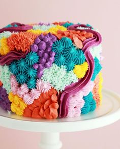 a multicolored cake sitting on top of a white plate with frosting flowers