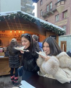 two women are eating food outside in the snow