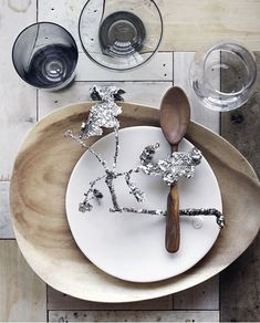 a white plate topped with silver foil and a wooden spoon next to two wine glasses