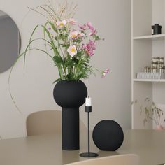 a black vase with flowers in it sitting on a table next to a white candle