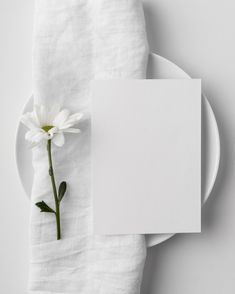 a white plate and napkin with a flower on it next to a blank paper sheet