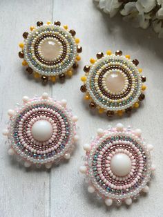 three beaded brooches are sitting on a table next to some white flowers