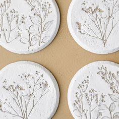 four white coasters decorated with pressed flowers on brown paper, sitting on a table