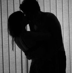 the silhouette of a man and woman kissing in front of vertical blinds with their arms around each other