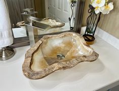 a bathroom sink sitting on top of a white counter next to a mirror and flower vase