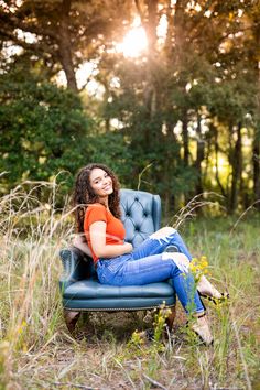 a woman sitting on a blue chair in the middle of some tall grass and trees