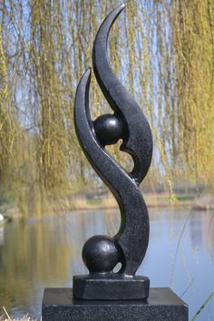 a black sculpture sitting in front of a body of water