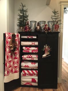 a black cabinet with red and white quilts on it next to a christmas tree