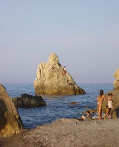 two people standing on rocks near the ocean