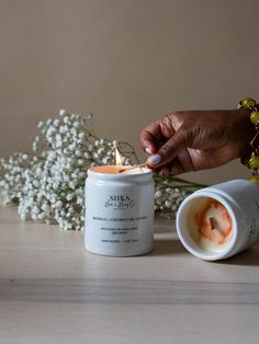 a person lighting a candle in a jar next to some baby's breath flowers