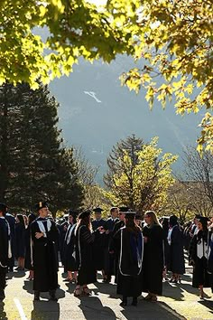 a group of people in graduation gowns standing on a road with trees and mountains behind them