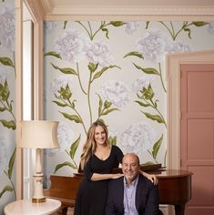 a man and woman pose for a photo in front of a floral wallpaper