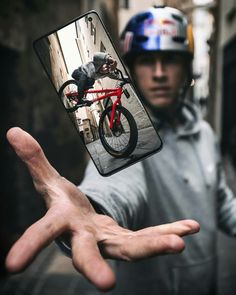 a man holding up a cell phone with a bicycle on it's back and his hand in front of him