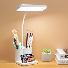 a white desk lamp sitting on top of a wooden table next to books and pencils