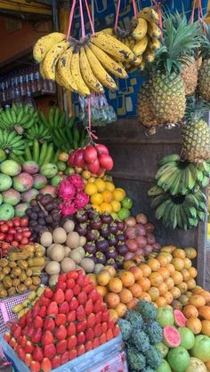 various fruits and vegetables are on display at a fruit stand with bananas, pineapples, oranges, melons, etc