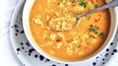 a bowl of macaroni and cheese soup with a spoon in it on a blue and white plate