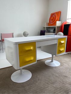 a white desk with two yellow drawers on top of it in a living room next to a red chair