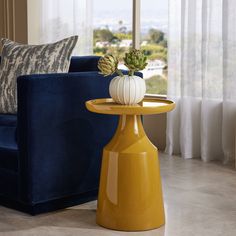 a living room with a blue couch and yellow side table in front of a window