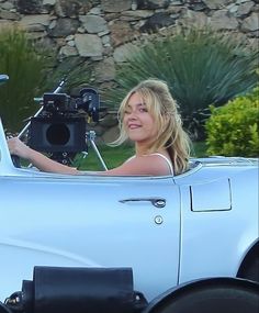 a woman sitting in the driver's seat of a white car with a camera