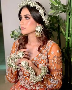 a woman in an orange dress is holding some flowers and wearing white beads on her head