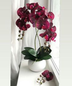 a white vase filled with purple flowers next to a window