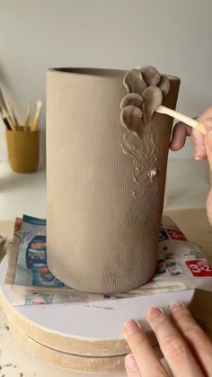 a person is painting a vase with flowers on the outside and inside, while another hand holds a paintbrush in their other hand