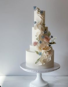 a three tiered white wedding cake with flowers on the top and sides, sitting on a pedestal