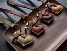 four leather heart shaped key chains on a wooden tray with brown and tan straps hanging from them