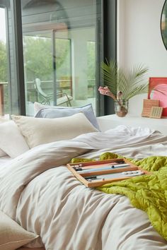 an unmade bed with pillows and blankets on it in front of a large window