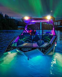 a boat with lights on is in the water under an aurora borel sky filled with green and purple lights