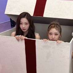 two young women are peeking out from behind a box with red and white stripes on it