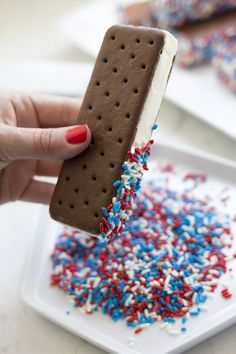 a hand holding an ice cream sandwich with sprinkles and red white and blue