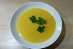 a white bowl filled with yellow soup and garnished with parsley on top