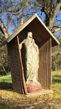 a statue in the shape of a woman standing next to a wooden structure with grass and trees behind it