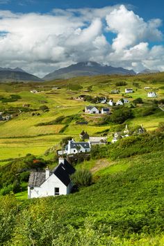 a green field with houses and mountains in the background