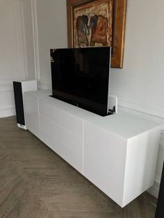 a flat screen tv sitting on top of a white entertainment center next to a painting