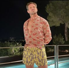 a man standing in front of a swimming pool wearing yellow and red swim trunks with pineapples on them