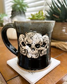 a coffee cup with a skull on it sitting on a table next to a potted plant