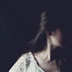 a woman with long hair wearing a white shirt and looking off to the side in dark room