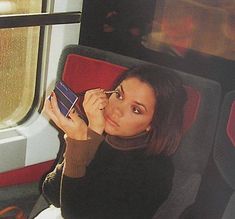 a woman sitting on a train holding a cell phone to her ear and looking at the camera