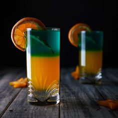 two glasses filled with liquid and orange slices on top of a wooden table next to each other