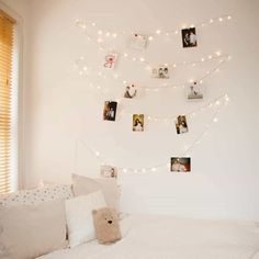 a white bed topped with lots of pillows next to a window covered in pictures and lights