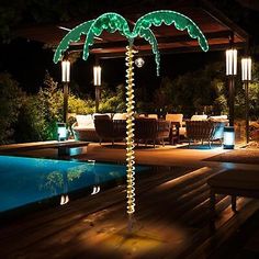 a lighted palm tree next to a swimming pool at night with lights on the deck