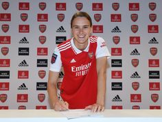 a female soccer player posing for a photo in front of a wall with red and white logos