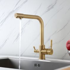 a faucet running water over a kitchen sink with apples on the counter top