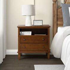 a nightstand with a clock on it next to a bed