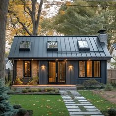 a small house with a metal roof and two windows on the front, surrounded by trees