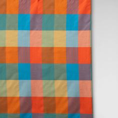 an orange, blue and green checkered blanket hanging on a wall in front of a white background