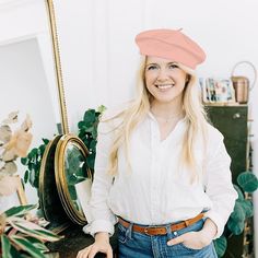 a woman standing in front of a mirror with her hands on her hips and wearing a pink hat