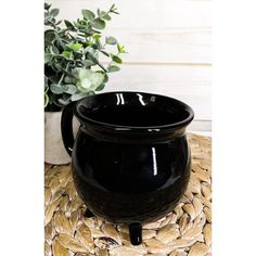 a black coffee mug sitting on top of a mat next to a potted plant